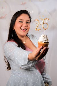 Smiling woman holding a cupcake with number 26 candles at her birthday celebration.